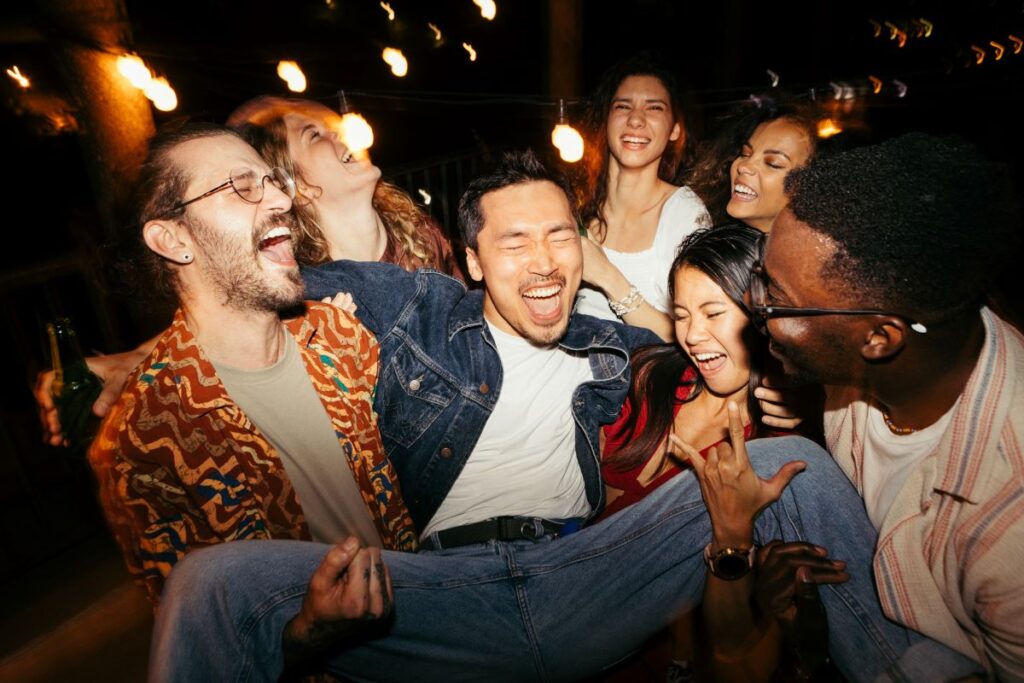 A group of friends gathered together laughing and lifting up one of their friends.