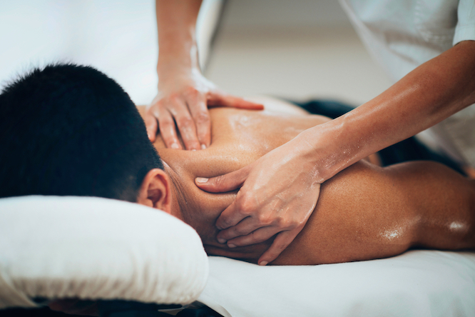 Sports massage. Massage therapist massaging shoulders of a male athlete, working with Trapezius muscle. Toned image