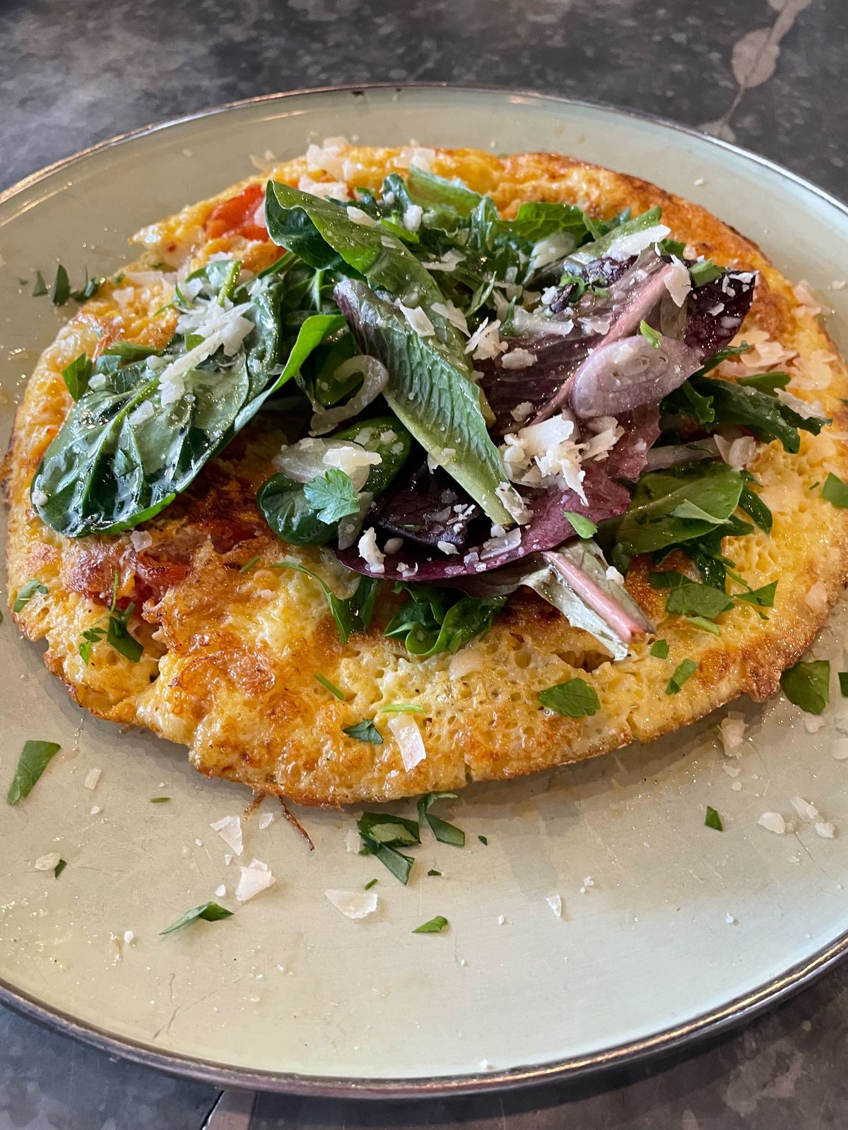 Vegetable frittata topped with fresh greens and shaved Parmesan